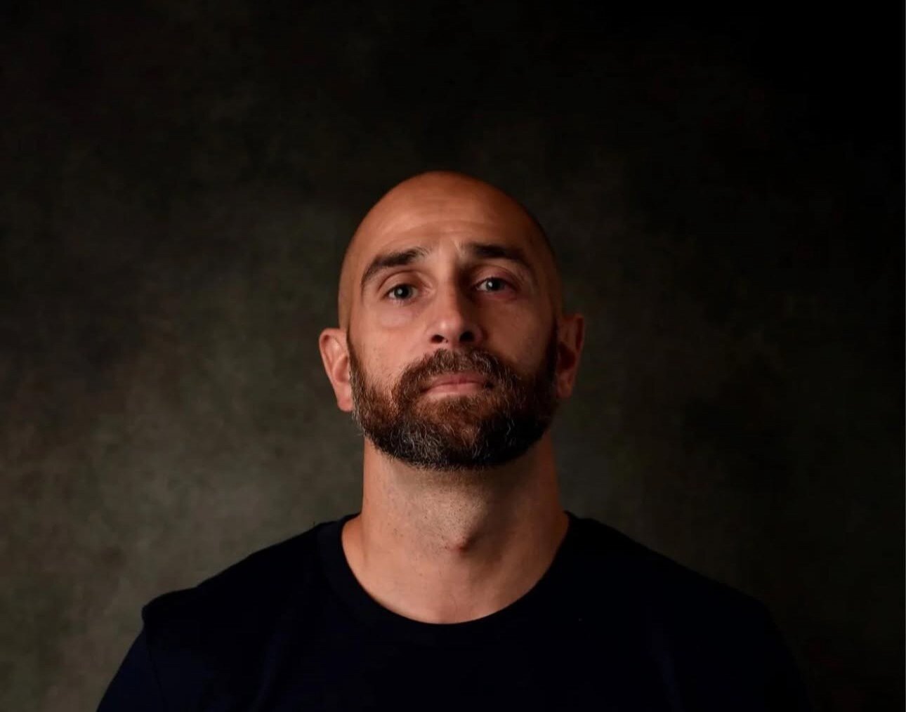 ThinkCyber's Head of Sales Seb Cameron wearing a black crew neck t shirt and is stood in front of a plain, dark background. 
